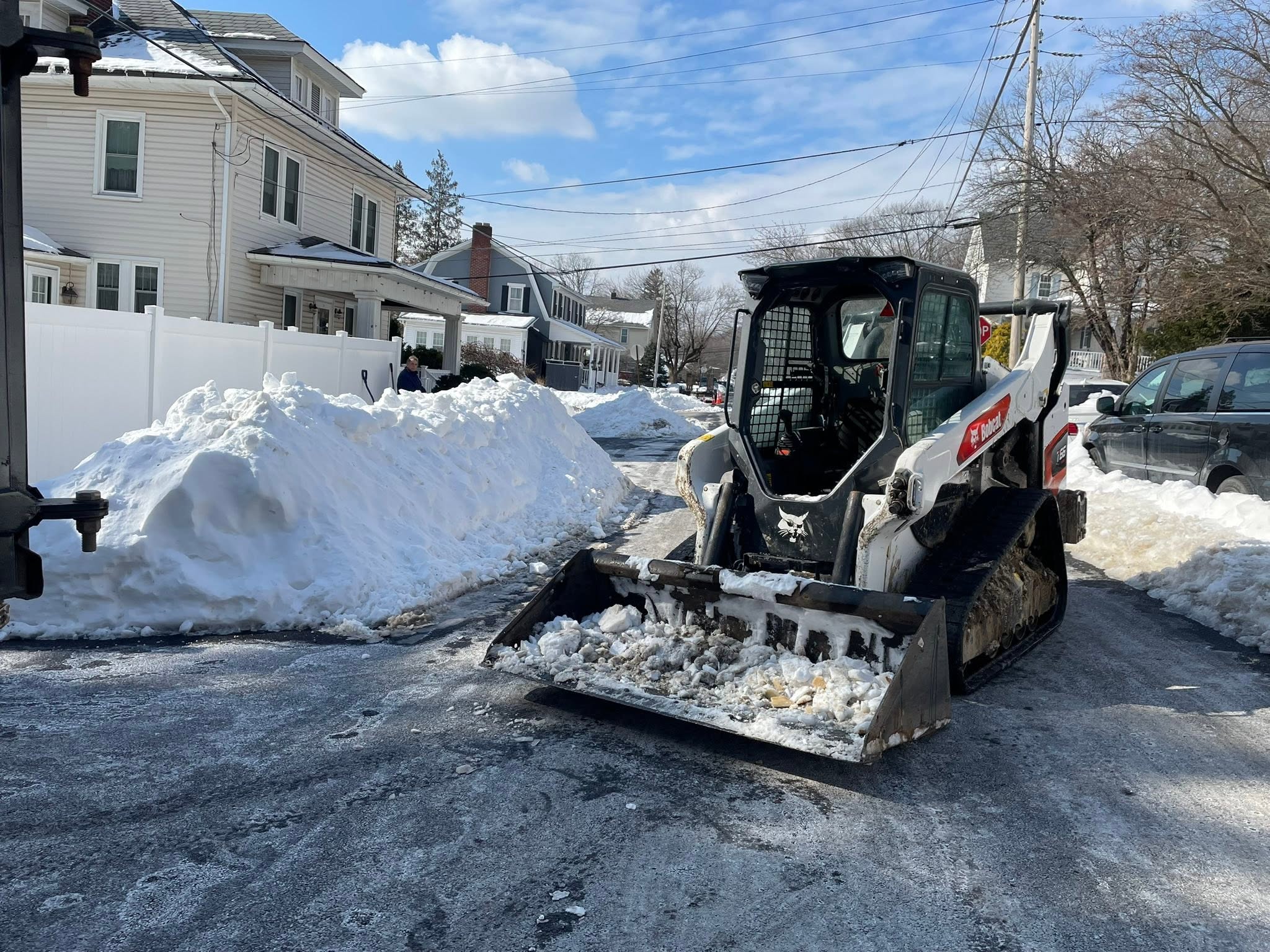 Bobcat skid steer scooping a bucket of snow in a driveway on a clear, sunny winter day