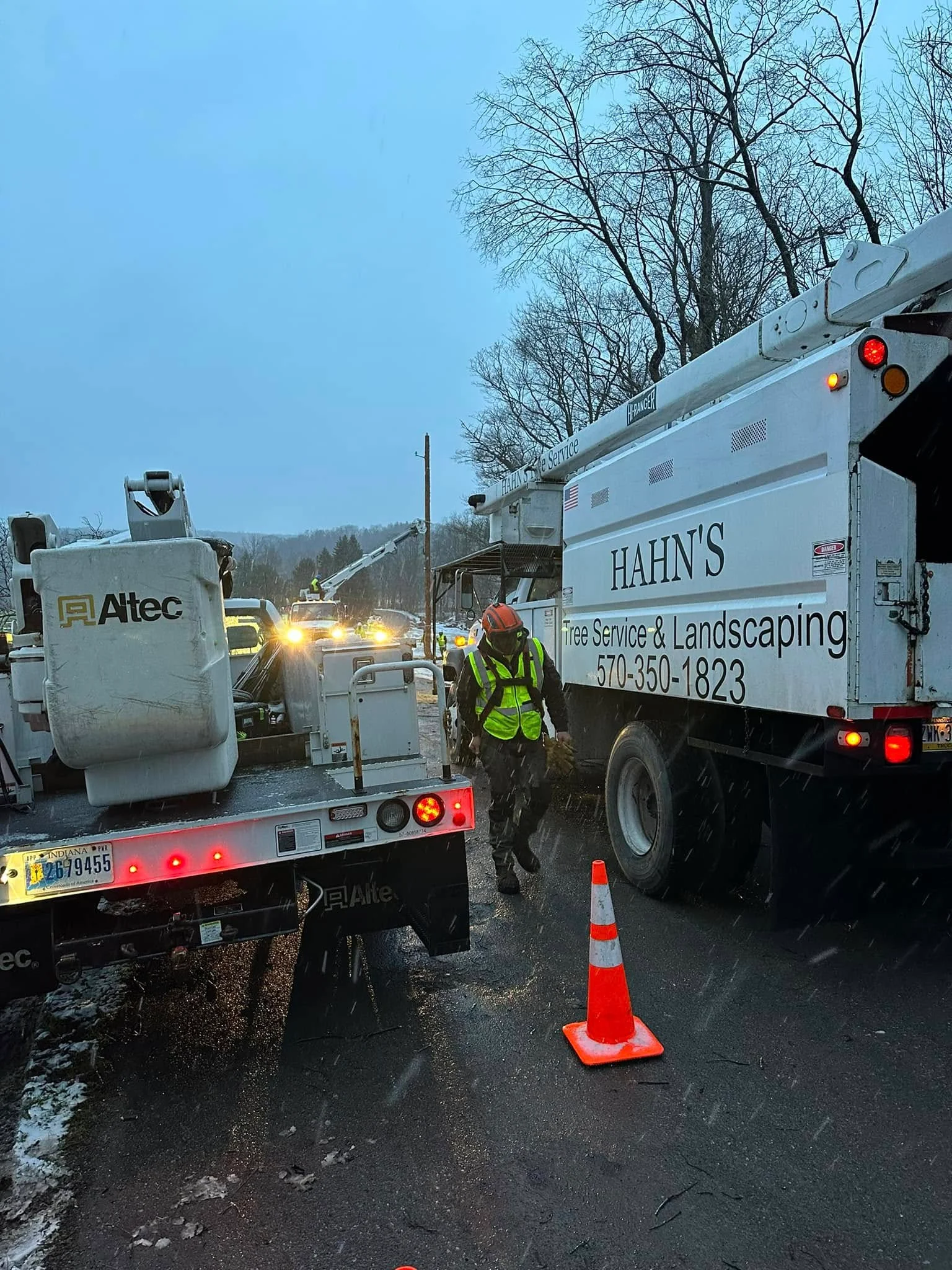 Worker beside a branded Altec truck on a snow-covered road during an emergency call