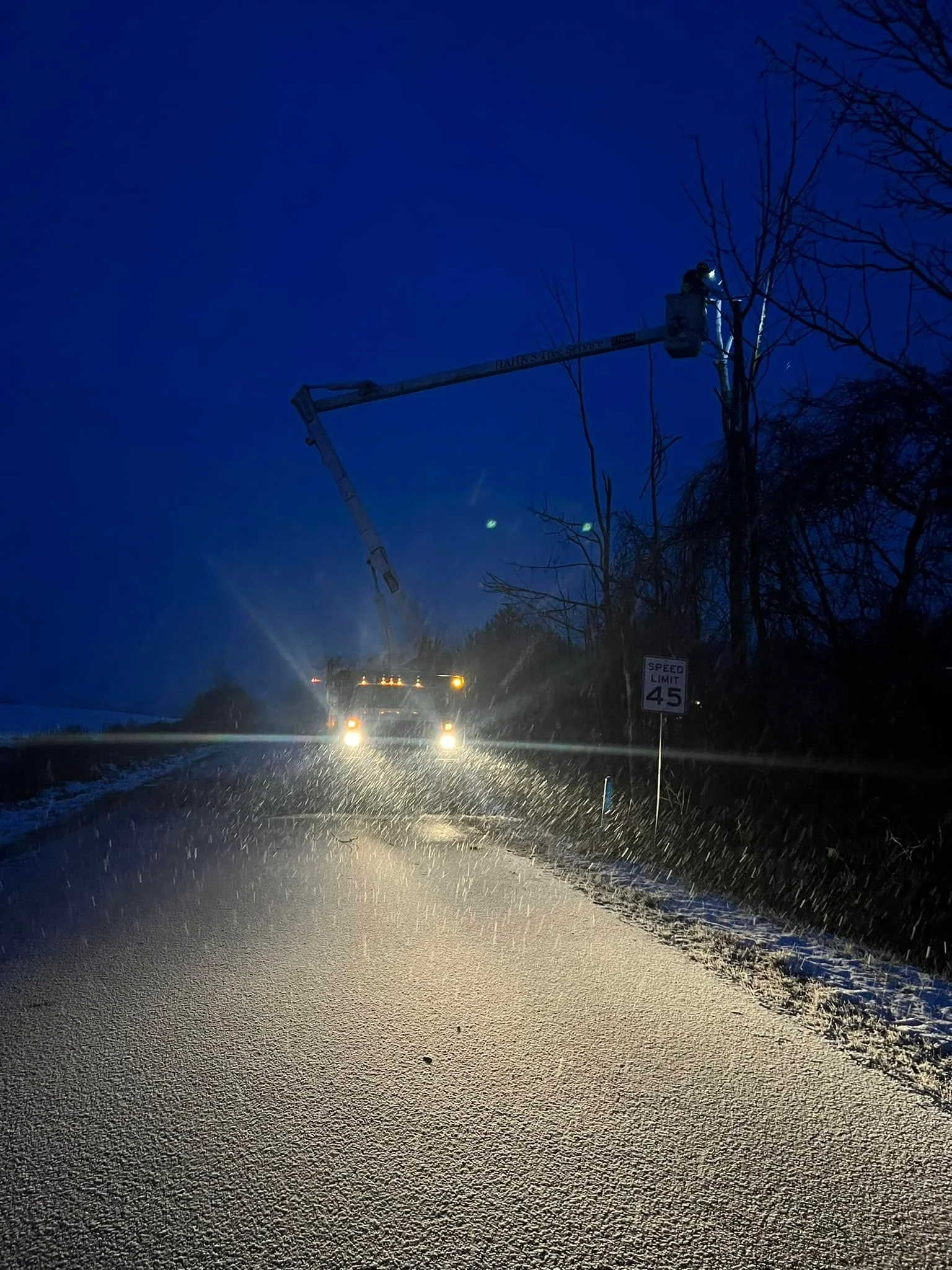 Bucket truck working under lights on a snowy road at night