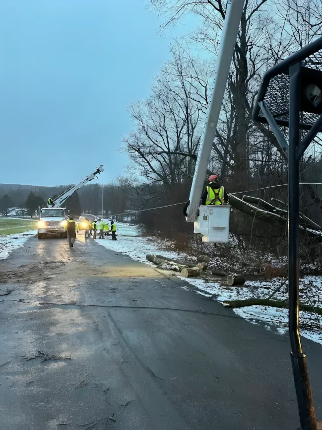 Two bucket trucks working an icy road beneath power lines after a storm