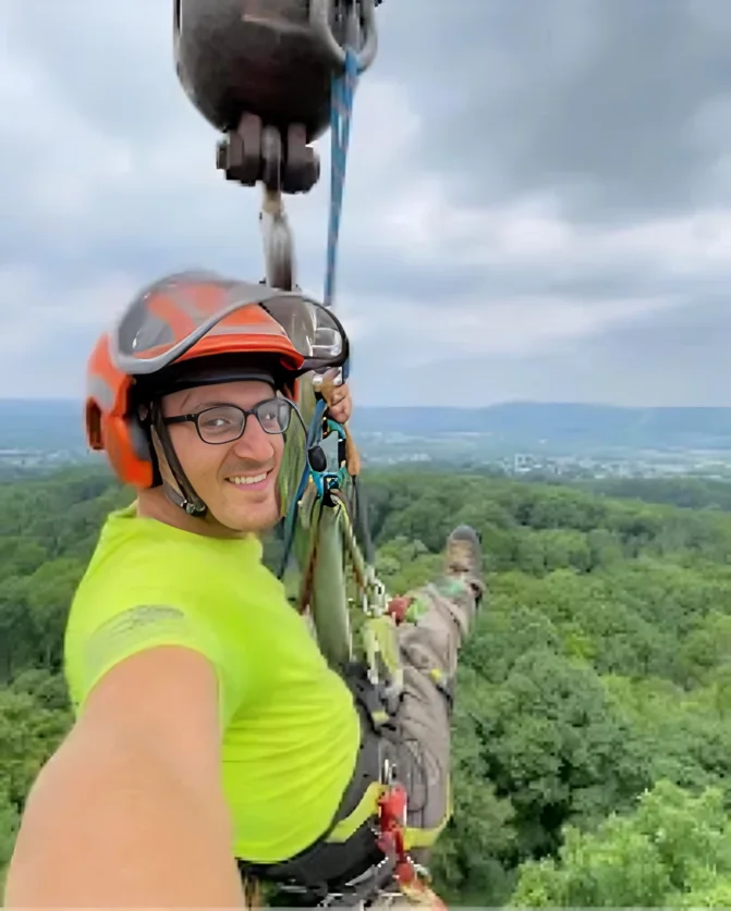 Hahn's Tree Service crew member rigged to the crane hook high above a forested valley near Brodheadsville PA