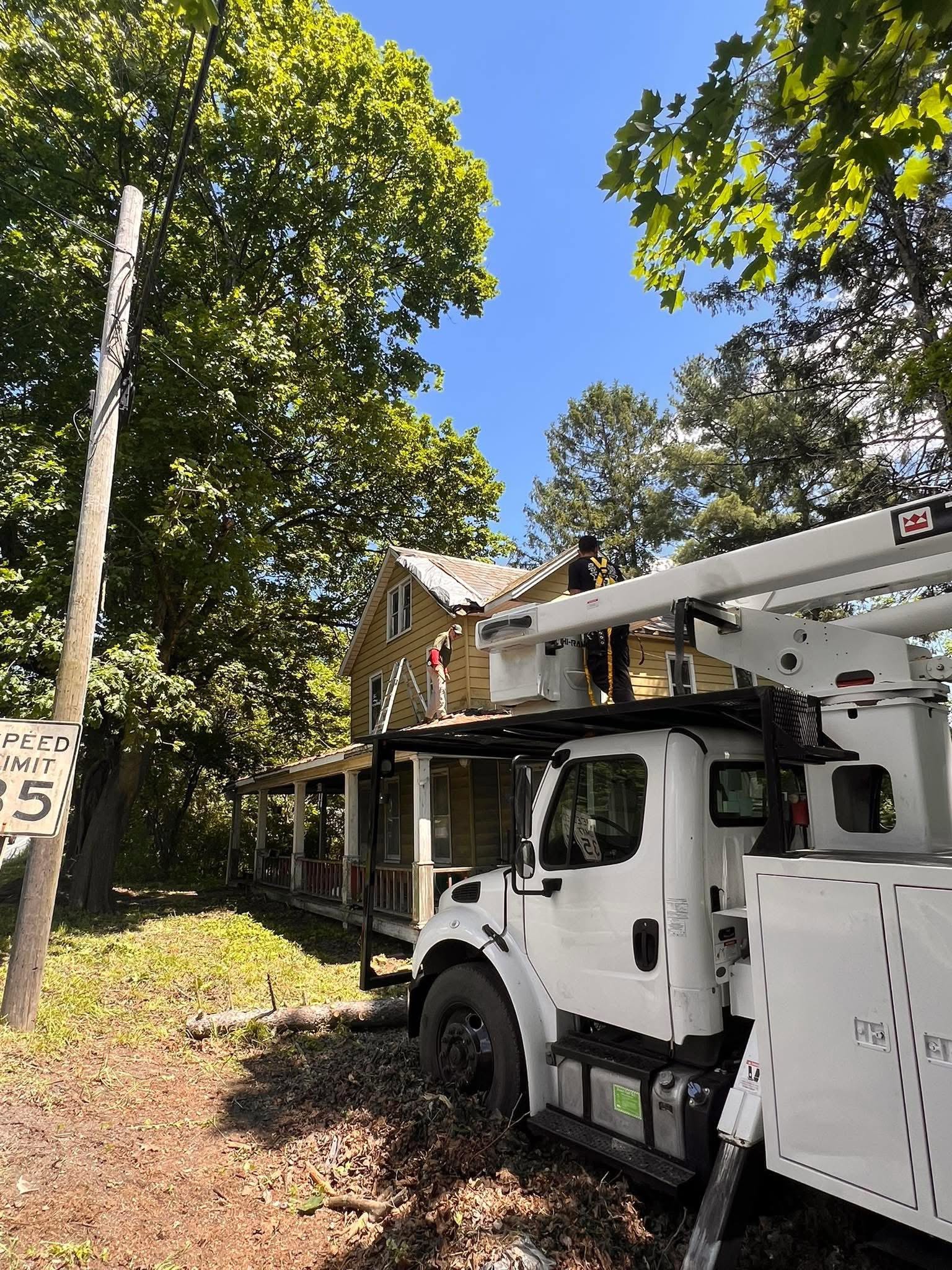 Hahn's Tree Service crew elevated on a roof with the bucket truck boom extended alongside a farmhouse